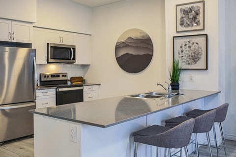 a kitchen with stainless steel appliances and a counter with three chairs