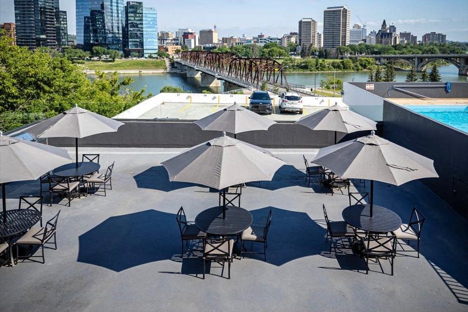 a rooftop patio with tables and umbrellas and a pool and a city skyline