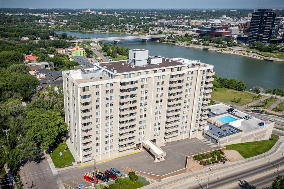A large white apartment building with a pool and a parking lot in front.