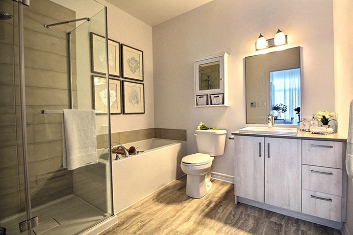 Spa like bathroom featuring standing, glass door shower and soaker tub at La Voile Broisbriand apartments