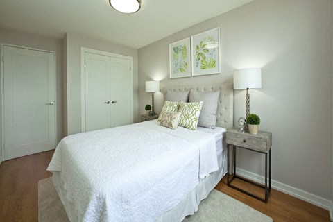 A bedroom with a white bed and a small table with a plant on it.