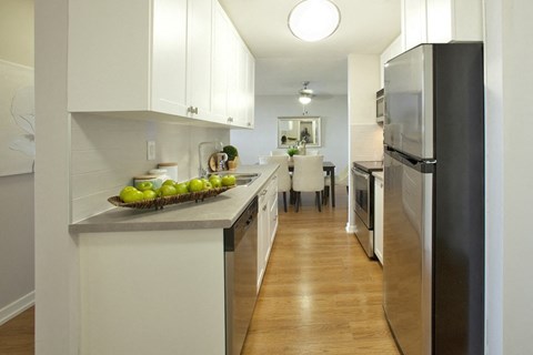 A kitchen with a refrigerator on the right and a counter with fruit on it.