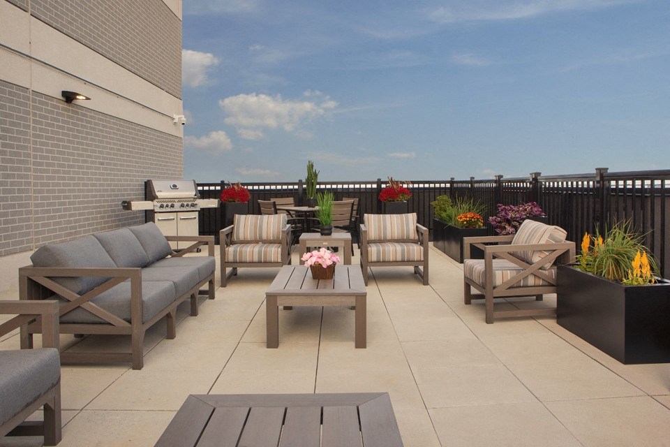 Rooftop terrace with cushioned patio seating and a BBQ seen in the background at Bayfield Tower Apartments in Barrie, ON
