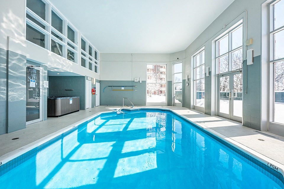 Bourg du Village indoor pool with high ceilings and floor to ceiling windows and patio door leading to outdoor patio area in Sainte Therese, QC