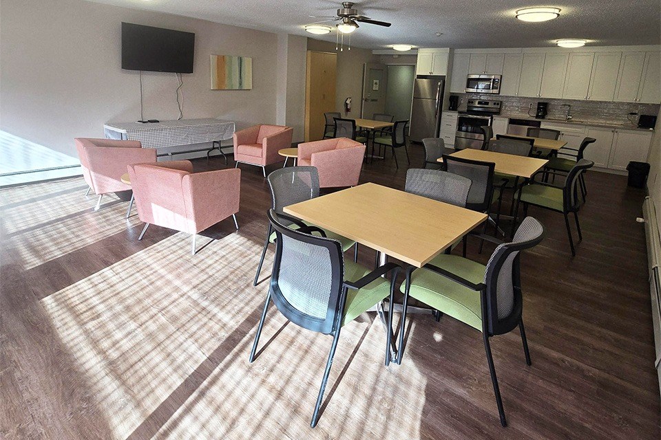 Social room with couch, tables, chairs, and stainless steel appliances at Brockville Apartments in Brockville, ON