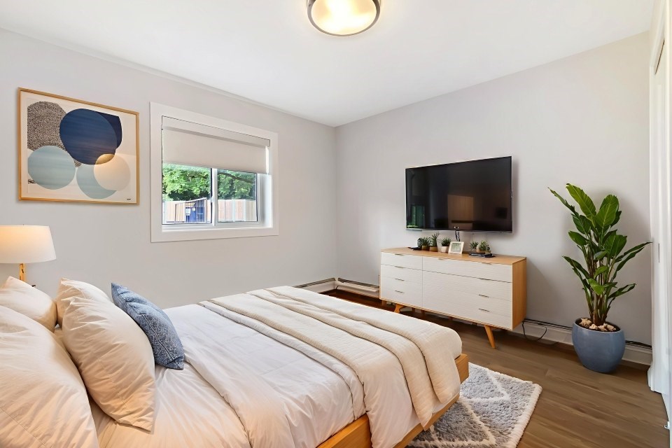 A bedroom with a bed, a dresser, a plant, and a painting on the wall.