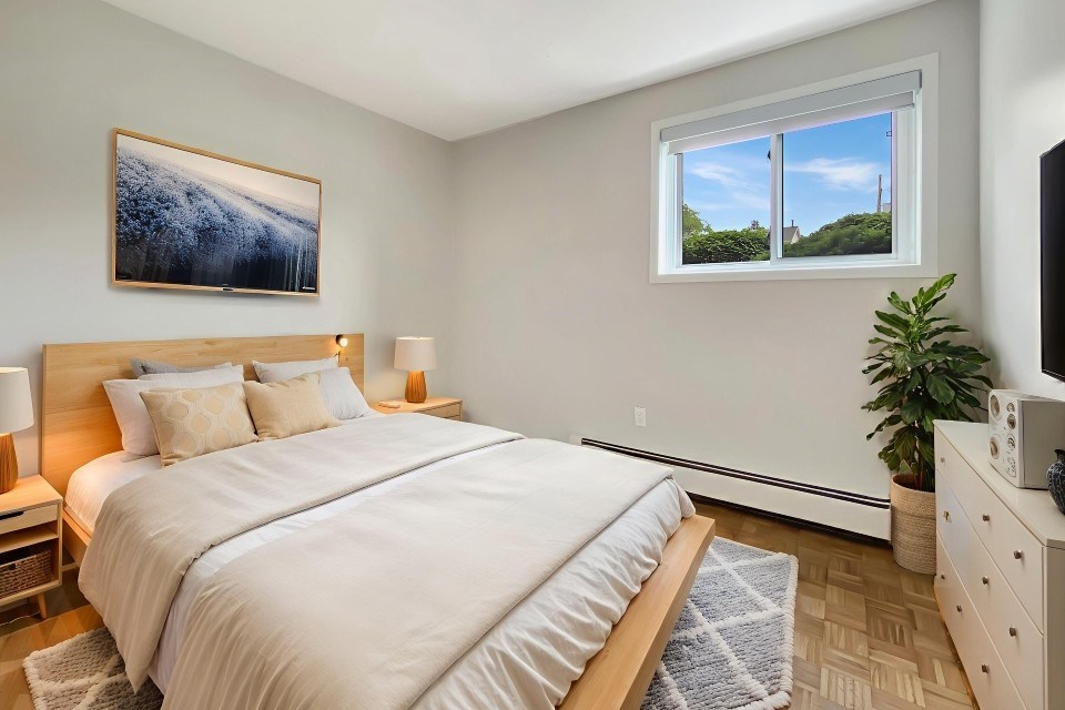 A bedroom with a large bed, a painting on the wall, and a window with a view of the outside.