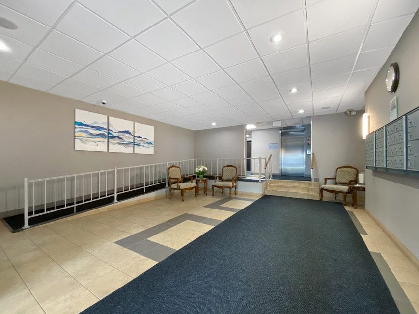 A hallway with a blue carpet and chairs on the side.