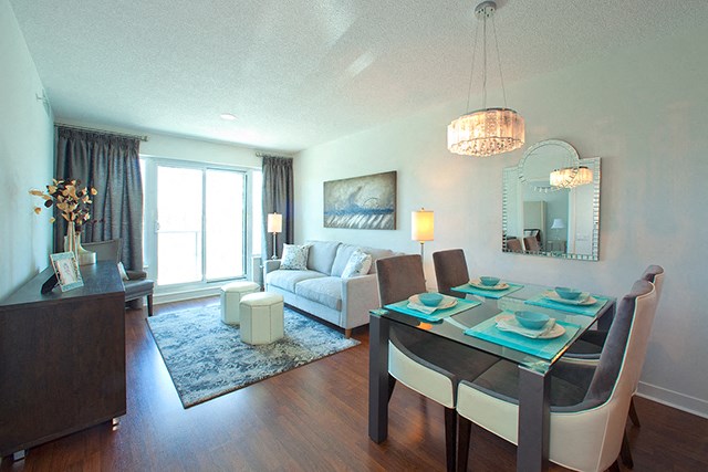 Dining room with set table and a blue table cloth. Living room is behind with a view of the patio at Cityview Apartments in Brampton, ON