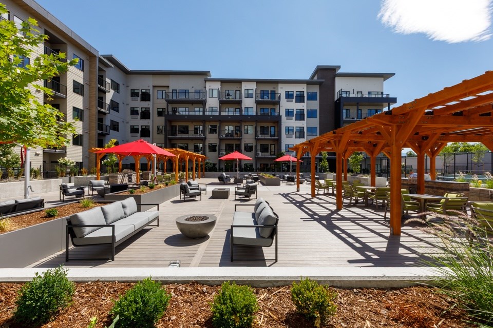 A sunny day at a modern outdoor seating area with red umbrellas and wooden pergolas at The Ambrosi in Kelowna, BC.