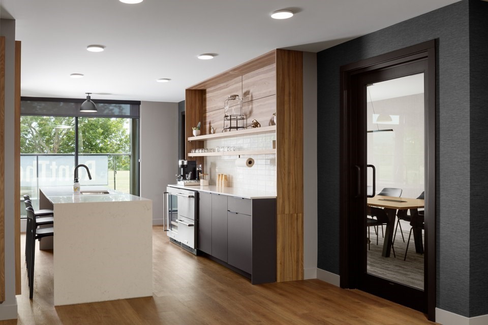 A conference room with a modern kitchen with a bar area and a dining table at The Ambrosi in Kelowna, BC.