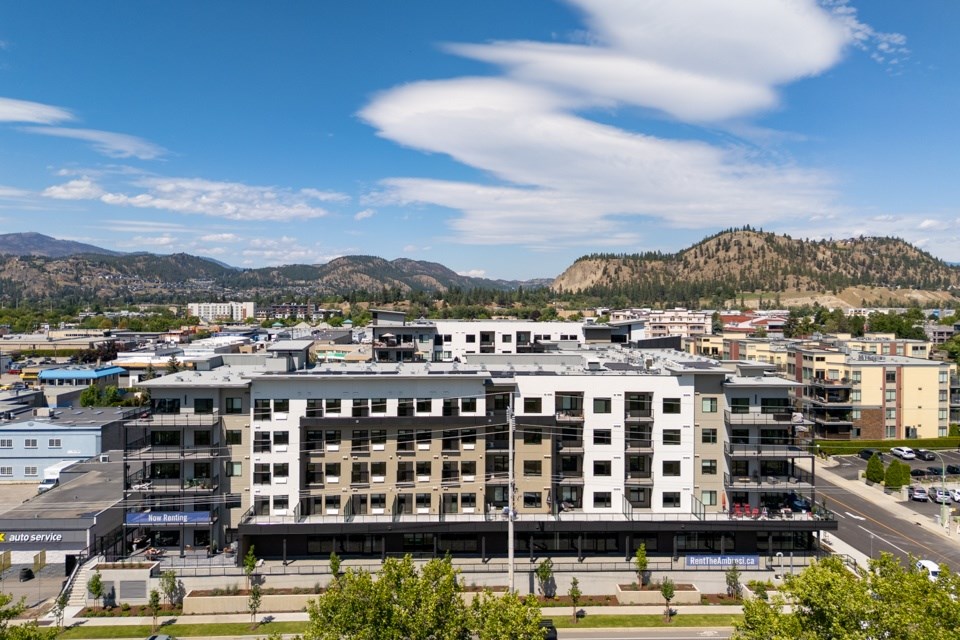 A large white building with a black roof is in the foreground of a cityscape.