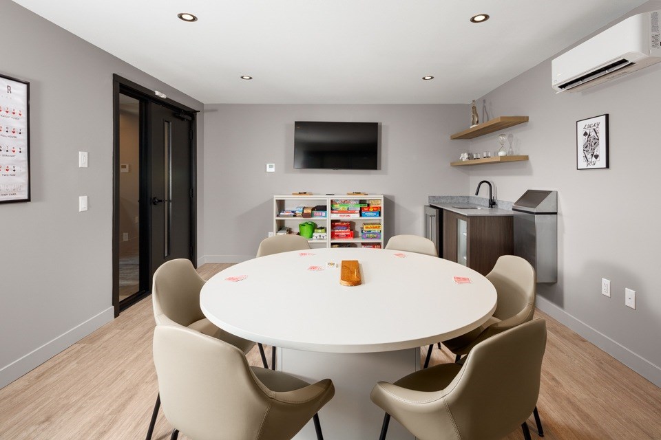 A games room with a white round table with four chairs around it at The Ambrosi in Kelowna, BC.