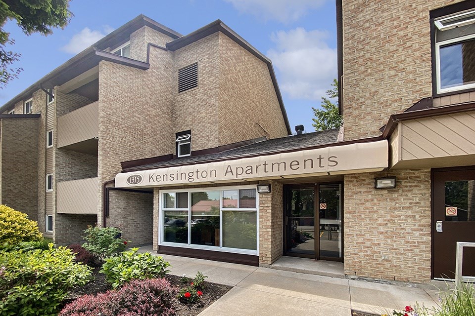 The image shows the front entrance of Kensington Apartments with a clear sky in the background.
