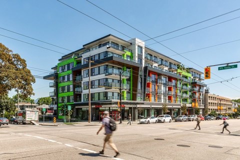 A street view of a multi-story building with a green and orange facade at 388 Kaslo East Village Apartments.