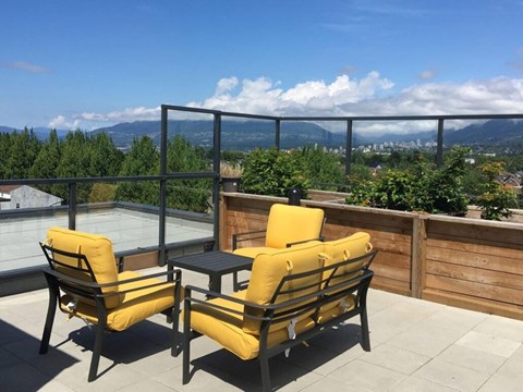 Two yellow chairs are on a patio with a table and a view of the mountains at 388 Kaslo East Village.