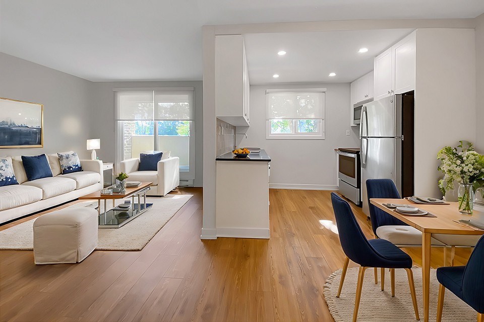 A modern living room with a white sofa, a glass coffee table, and a dining table with chairs.