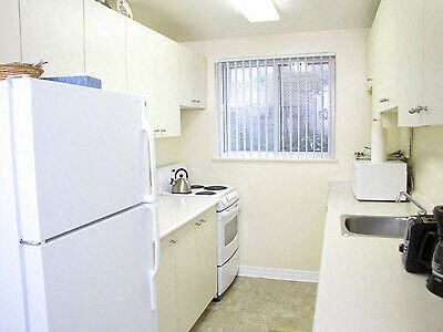 A small kitchen with white appliances and a window with blinds.