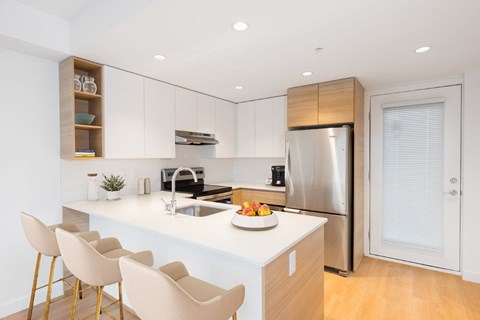 A modern kitchen with a stainless steel refrigerator, sink, and bar stools at 388 Kaslo East Village.