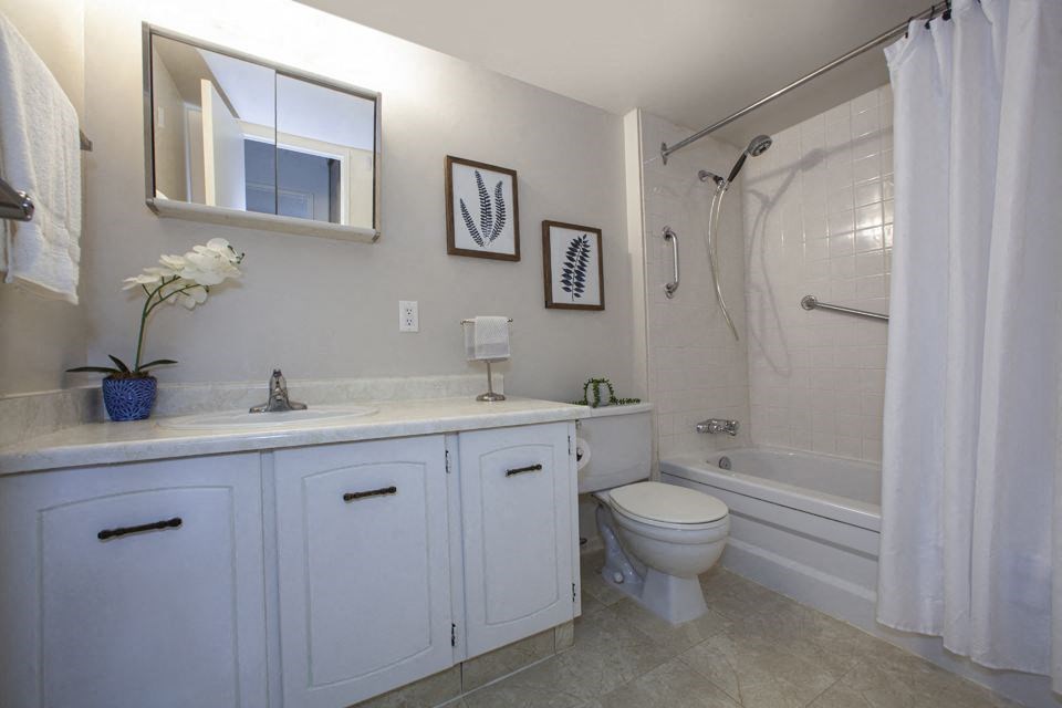 Bathroom with a large, three-door vanity, toilet and bathtub with a shower head on hose in a standard suite at Lorneville Apartments in Cornwall, ON