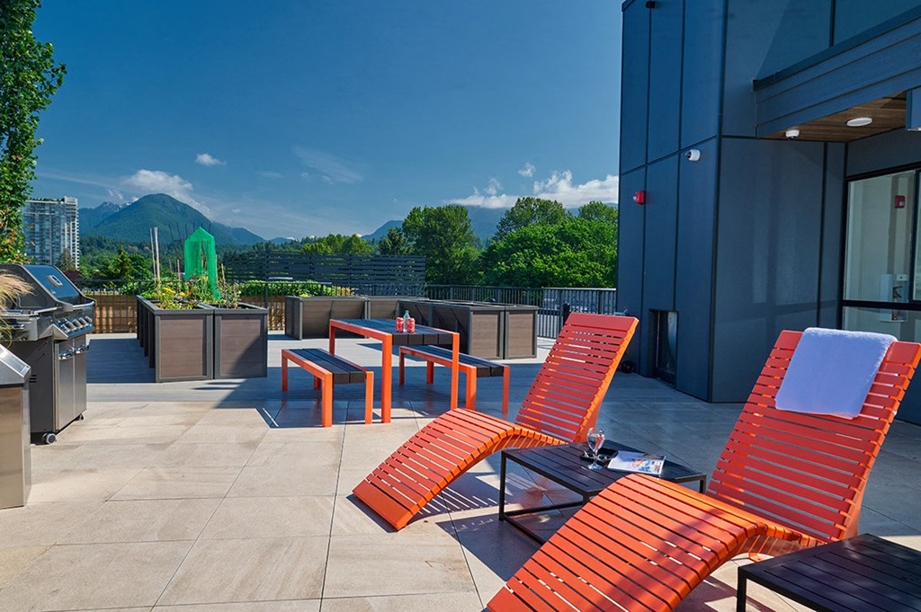a rooftop deck with lounge chairs and a grill