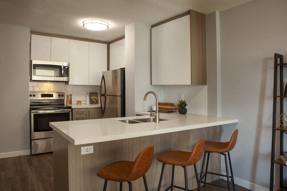 A kitchen with a white countertop and brown chairs.