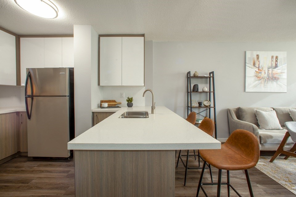 A modern kitchen with a white countertop and wooden chairs.