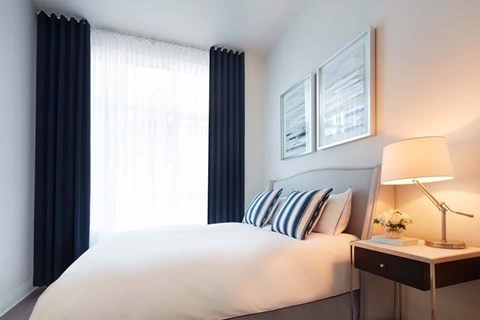A bedroom with a large bed, a nightstand with a lamp, and pictures on the wall.