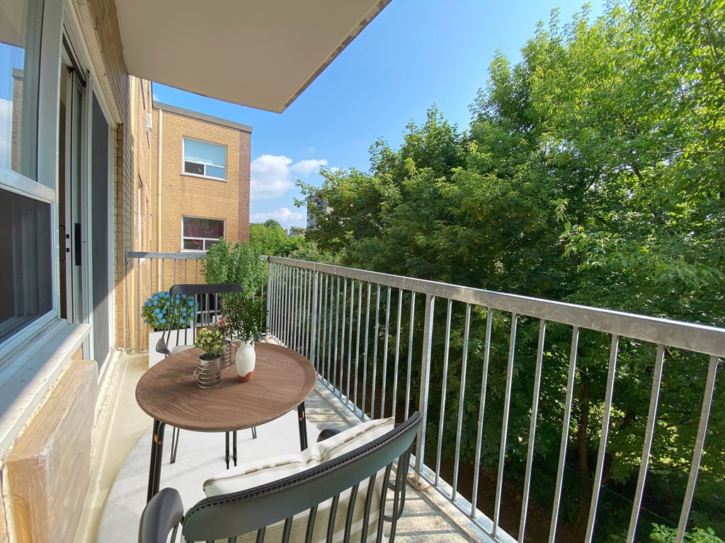 A balcony with a table and chairs overlooking a green tree.