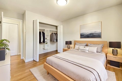A bedroom with a large bed and a wardrobe with clothes hanging on it at Moira Apartments in Belleville, ON