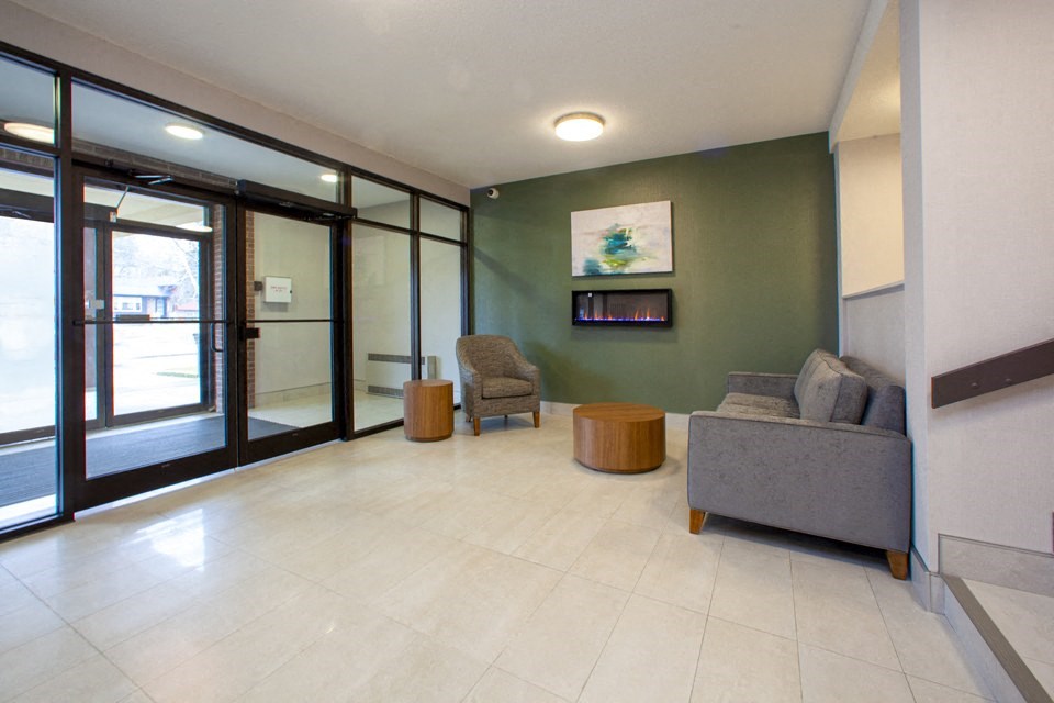 Lobby with a couch, a chair and side tables looking towards entry with floor to ceiling windows and doors at Northgate Tower Apartments in Woodstock, Ontario