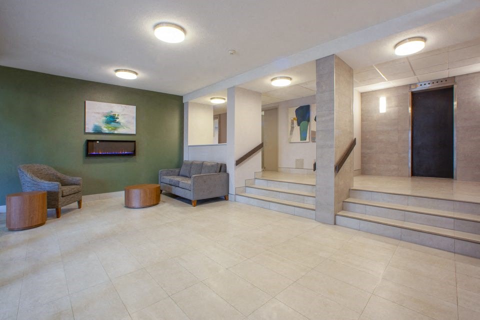 Lobby with lounge seating and staircase with elevators in the background at Northgate Tower Apartments in Woodstock, Ontario