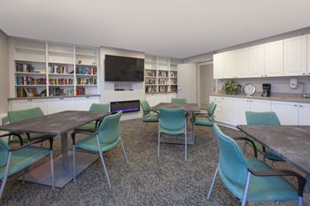Social room with tables and chairs, flat screen TV with a fireplace below and library at Northgate Tower Apartments in Woodstock, Ontario