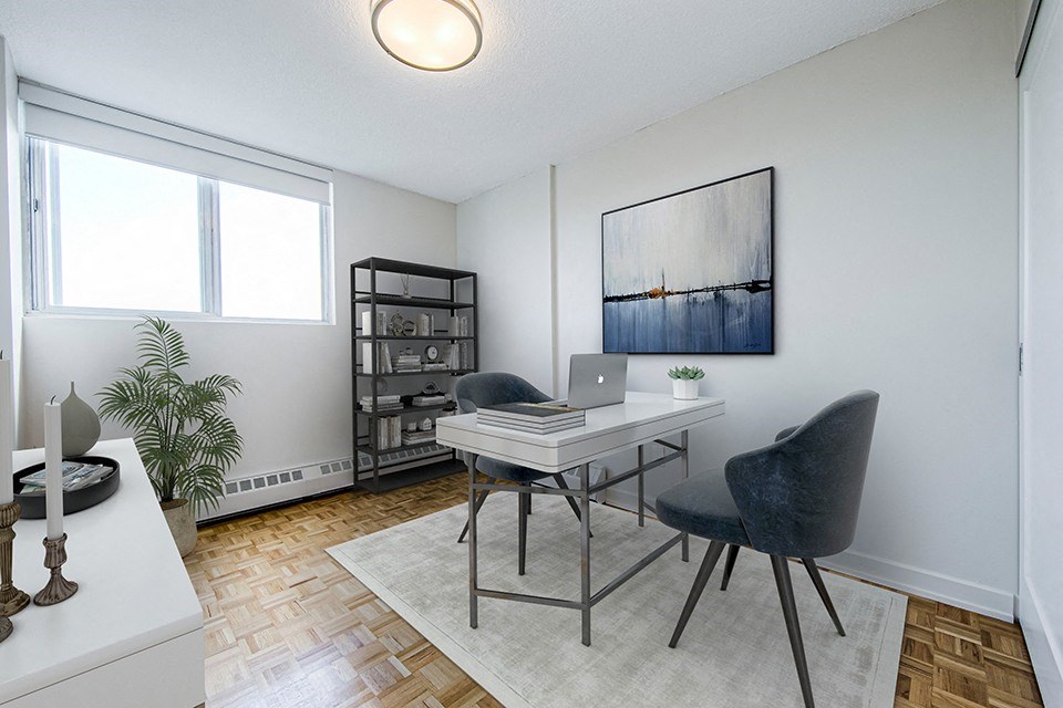 Second bedroom staged as an office with desk, chair on either side of desk and bookcase at Park Place Apartments in Bradford, ON