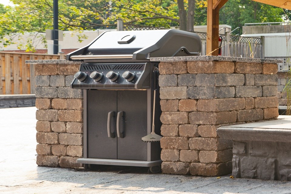 a bbq grill in a backyard with a stone wall