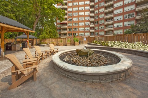 a firepit with wooden chairs around it and an apartment building in the background