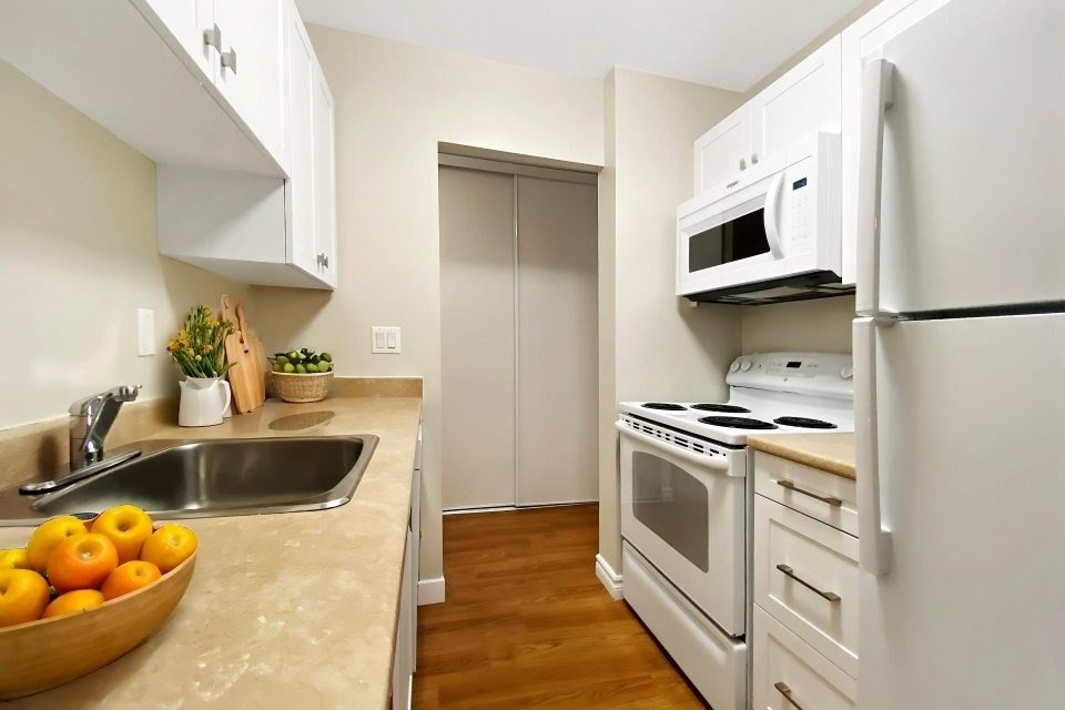 A kitchen with white appliances and a bowl of oranges on the counter.