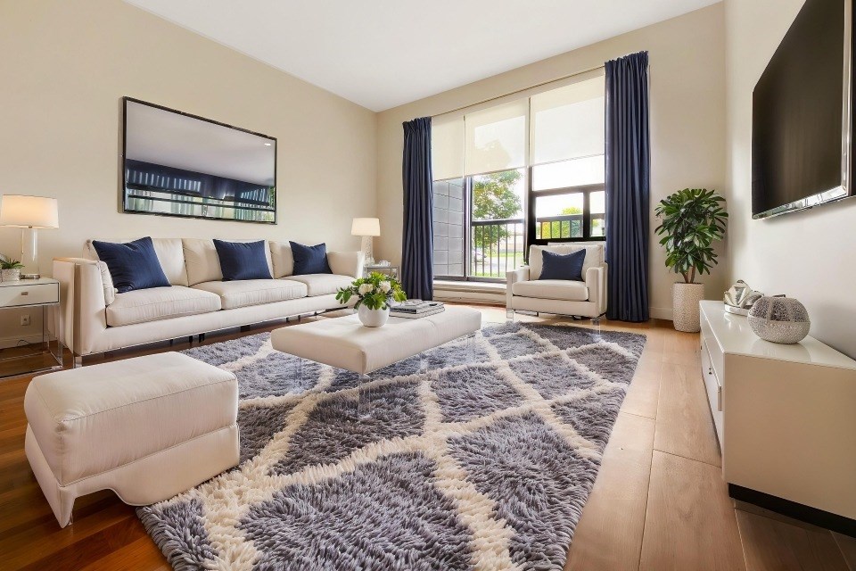 A modern living room with a white sofa, a grey rug, and a large window.