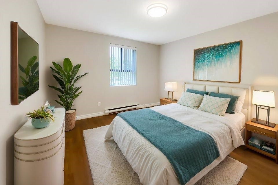 A bedroom with a bed, a nightstand, a plant, and a painting on the wall.