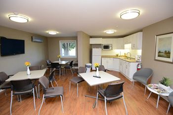 Social room with tables and chairs and a kitchen at Riverbend Tower in Chatham, ON