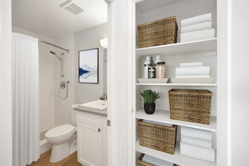 Linen closet with baskets and white towels with bathroom seen in the background at Riverbend Tower Apartments in Chatham, ON