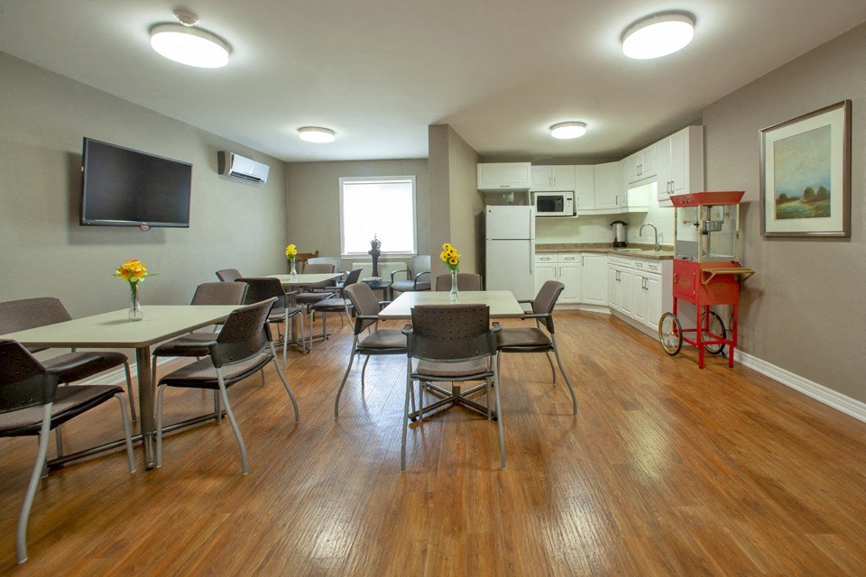 Social room with kitchenette ant tables and chairs at Riverbend Tower Apartments in Chatham, ON