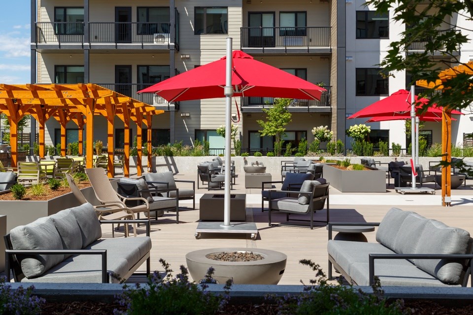 A patio with grey couches, red umbrellas, and a fire pit at The Ambrosi in Kelowna, BC.