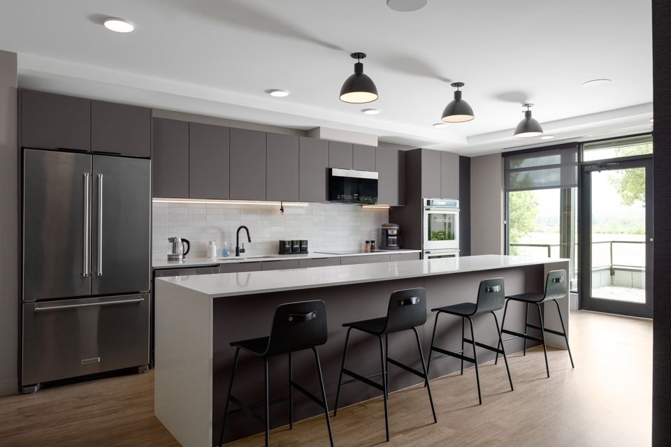 A modern social room with a kitchen area and three chairs at The Ambrosi in Kelowna, BC.