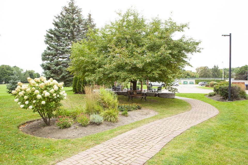 Sunnidale Place garden area with bench seating and patio in background in Barrie, ON