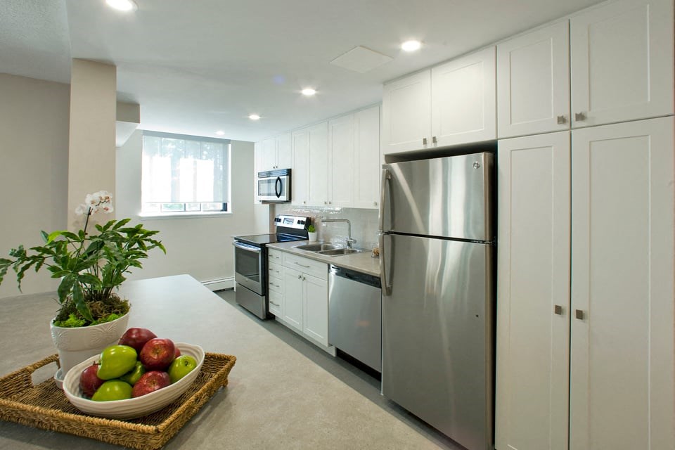 Sunnidale Place Finished kitchen with cupboards, washing machine, microwave, and stove. Apples sit in a bowl to the left in Barrie, ON