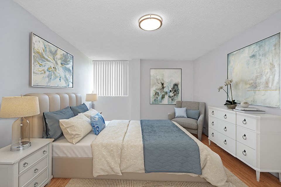 Sunset Towers primary bedroom with queen bed, two nightstands, dresser and armchair, looking towards window in St. Thomas, ON
