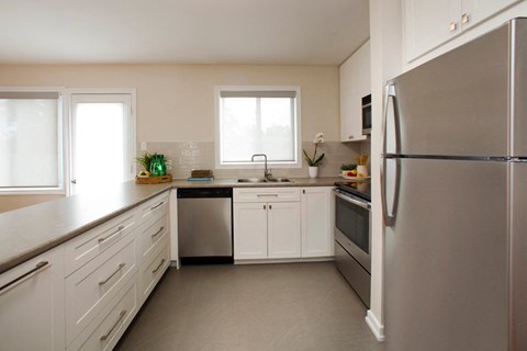 Cook like a professional in modern upscale kitchens Tamarack Woods Sleek modern kitchen with spotless counters, a fridge, sink, oven and washing machine. Easy view of the outdoor patio through the window and door in Barrie, ON