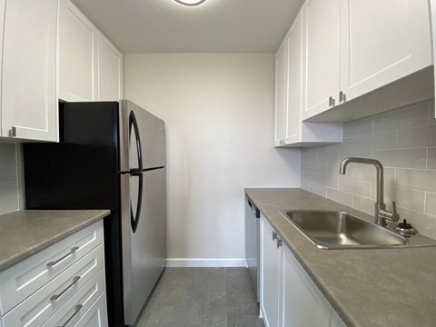 an empty kitchen with white cabinets and a black refrigerator