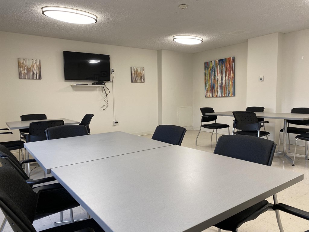 Resident social room with tables and chairs and flatscreen TV at Tarawood Place in Peterborough, ON